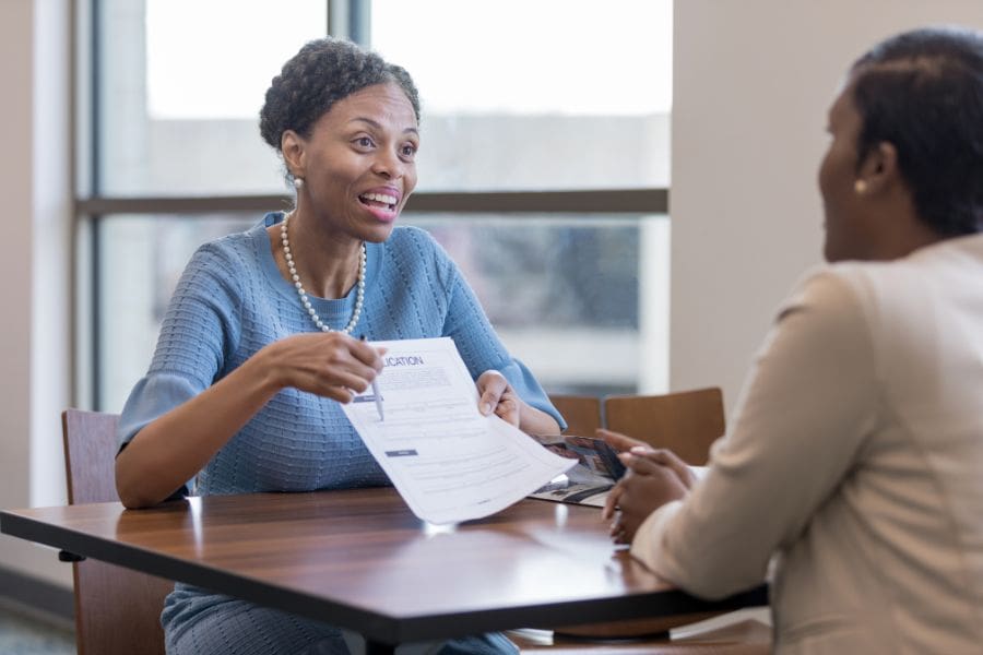 A woman is sitting across the desk from a financial advisor who is explaining how to get a credit card in Canada. 