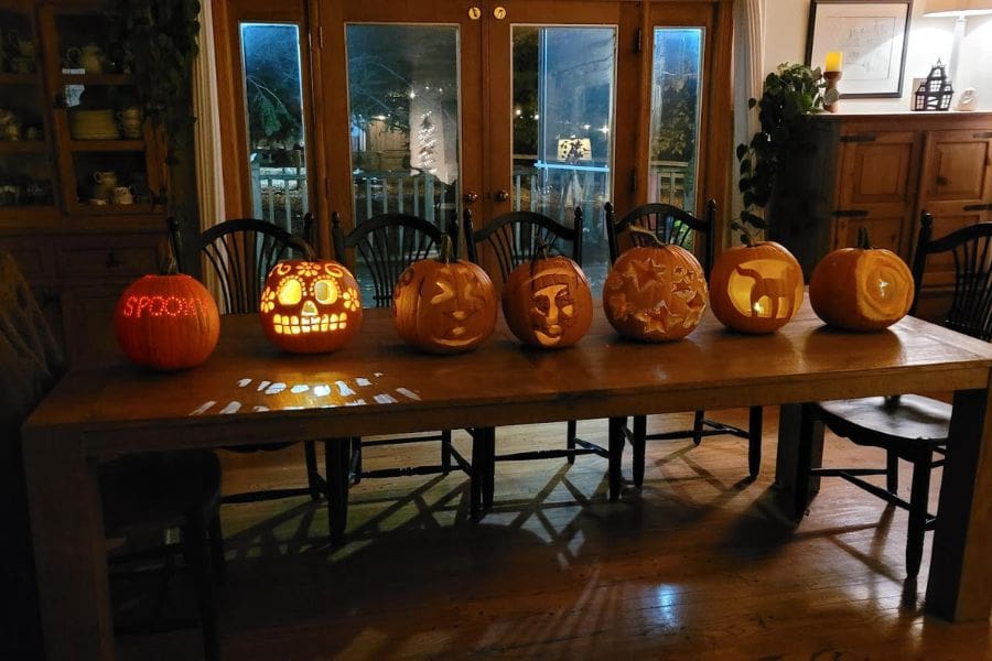 Seven carved pumpkins are displayed on a dining table. Carving pumpkins is a favourite Halloween tradition in Canada.