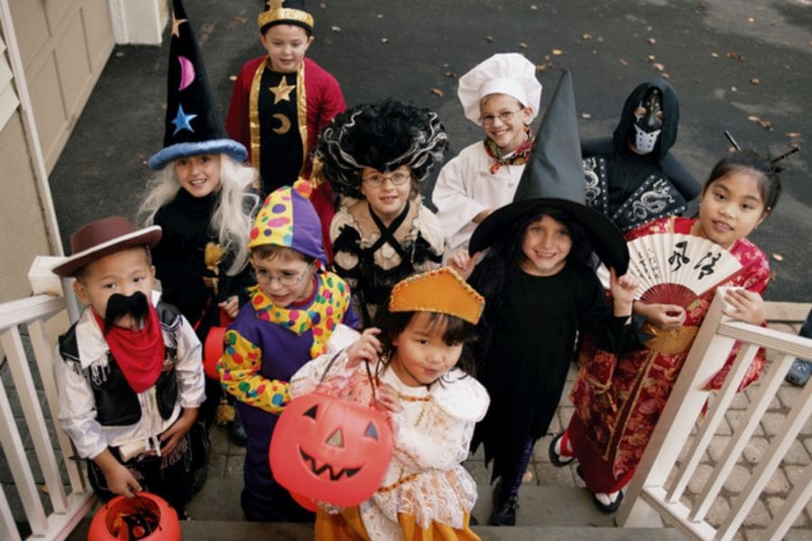 A group of excited young children are dressed in costumes and trick-or-treating at a home. 