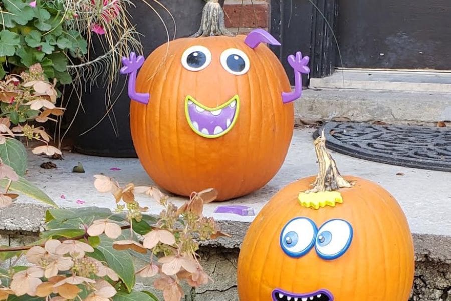 Two decorated Halloween pumpkins are placed at the front entrance of a home. 
