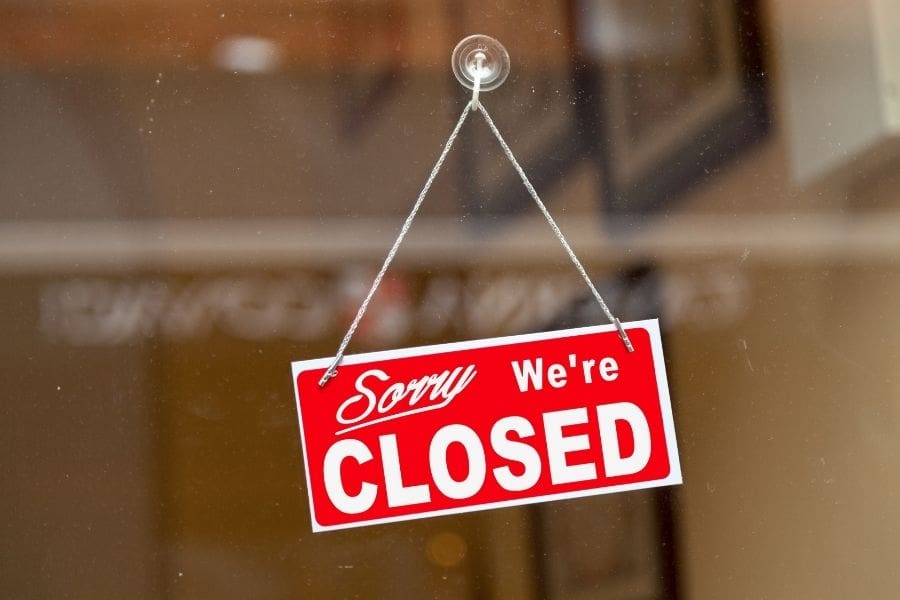 Red sign hanging on a glass door of a building saying "Sorry, we're closed".