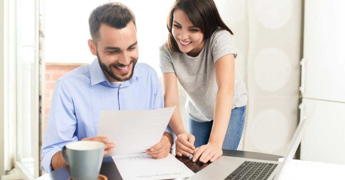 A newcomer couple in a modern Canadian home preparing their first time filing taxes in Canada using a laptop.