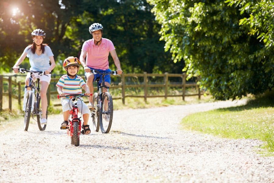 The Canada Child Benefit can help newcomers families with the cost of raising children in Canada. A family are riding bycyles in a park in Canada.