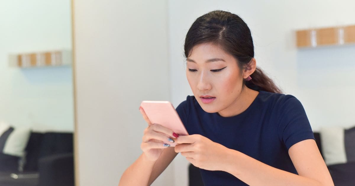 A woman is looking at a mobile phone displaying a suspicious text message requesting personal banking information, illustrating a phishing scam in Canada.
