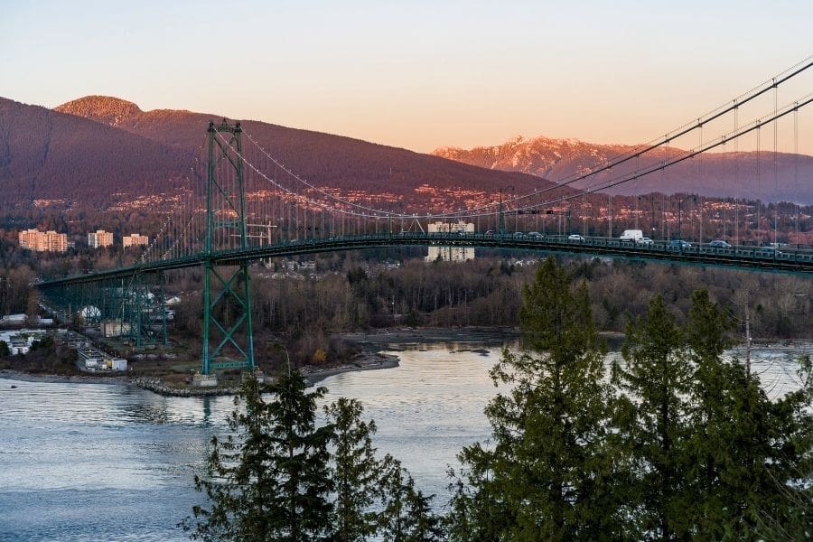Cars driving over the Lions Gate Bridge toward North Vancouver, British Columbia, with trees and mountains in the background.