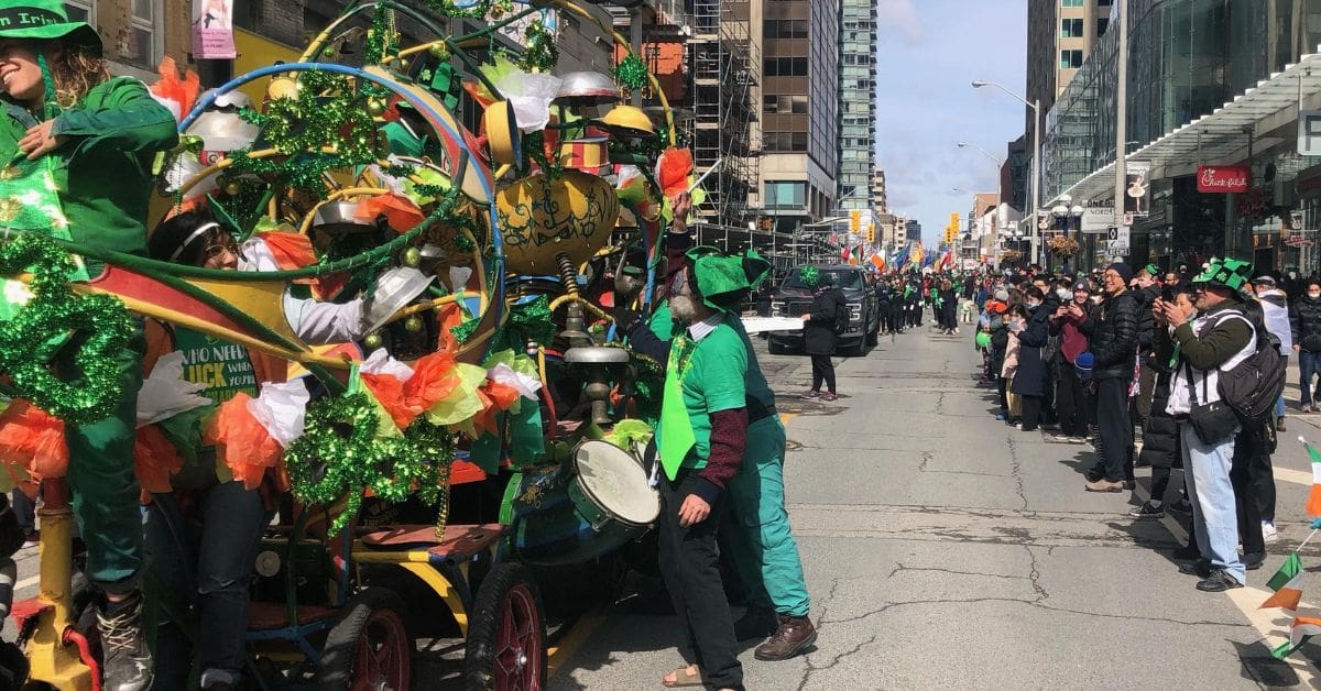 A diverse group of people of various ages and backgrounds smiling and wearing green accessories at the Toronto St. Patrick's Day Parade on Yonge Street.