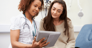 A woman doctor with a stethoscope around her neck shows a medical chart to a female patient who is sitting on an examination table. Travel medical insurance can help newcomers to Canada avoid medical visits and costs