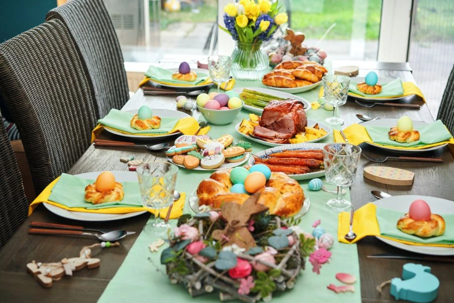 A dinner table with a traditional Canadian Easter dinner with a glazed ham, coloured eggs, spring tulips, and festive hot cross buns.