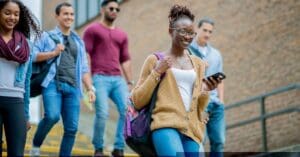 Multi-ethnic students are walking down the steps at a university campus in Canada. A smiling female African student is carrying a backpack and a mobile phone. With a GIC, students manage their finances, focus on studies, and reduce stress.