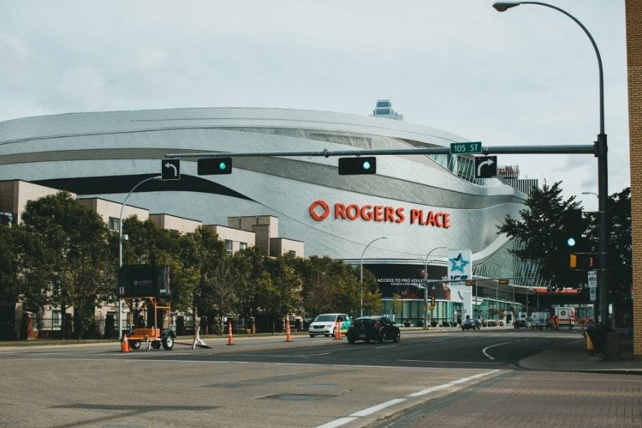 A street-level view of the modern, silver Rogers Place arena building in downtown Edmonton under a bright sky.