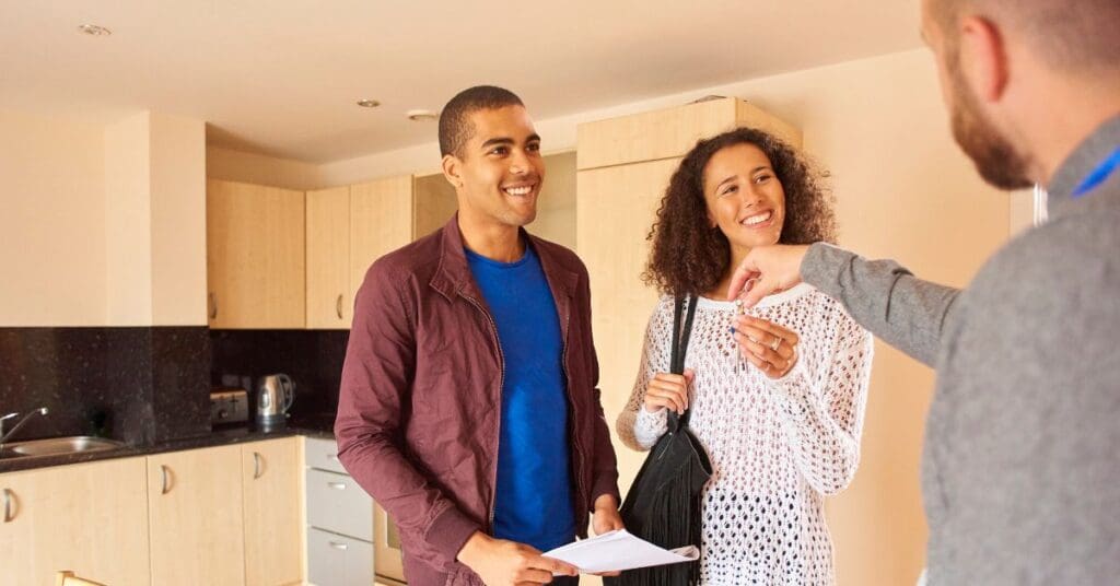A newcomer couple smiling as a landlord hands them apartment keys after their rental application was approved.