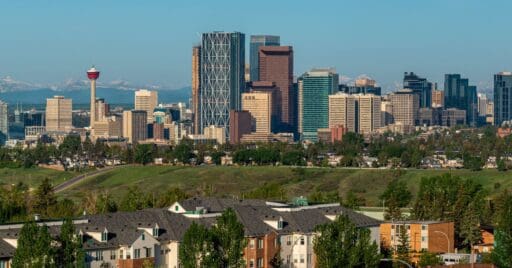 Panoramic view of the Calgary skyline and mountains on a bright summer day. Discover some of the best Calgary neighbourhoods for renting.