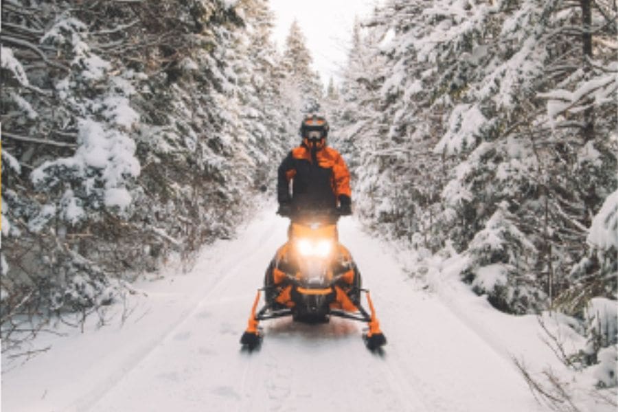 A person is riding on a snowmobile along a winter trail lined with snow-covered trees. 