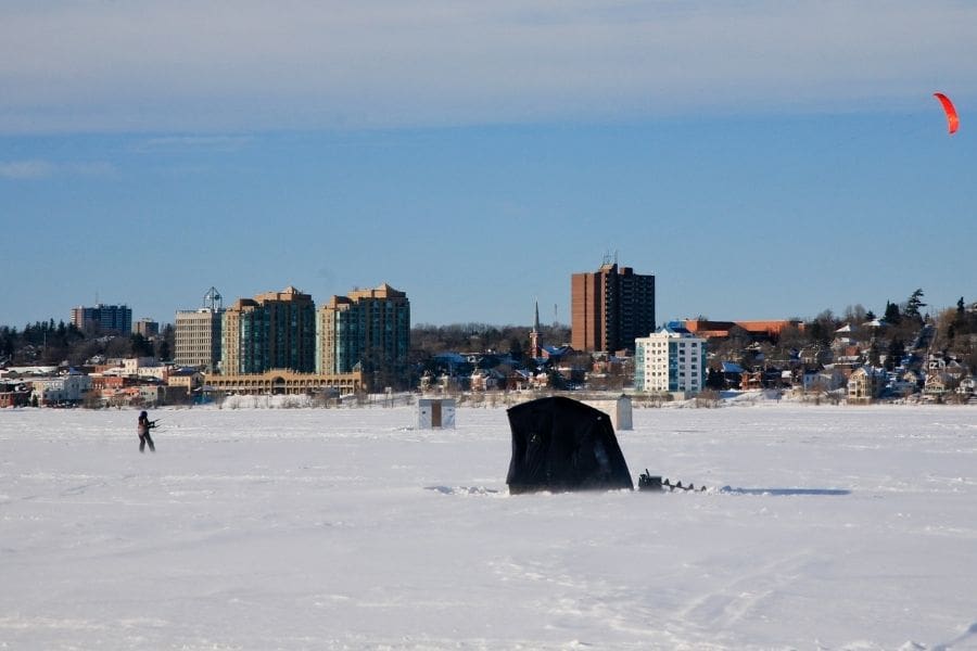 Ice fishing hut and snow-kiter on frozen Kempenfelt Bay with downtown Barrie city centre high-rise condos in the background.