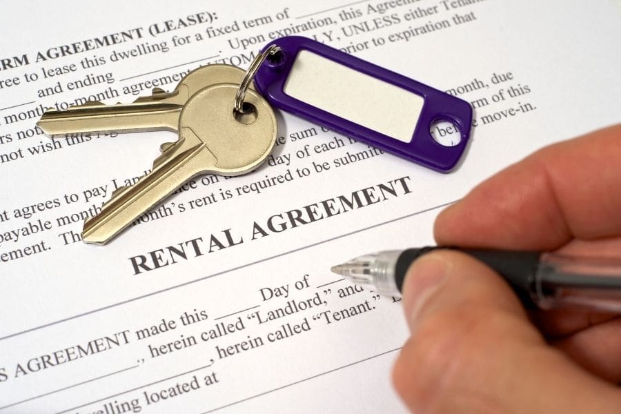 A tenant is signing a rental agreement with a landlord. Apartment keys are on top of the document. 