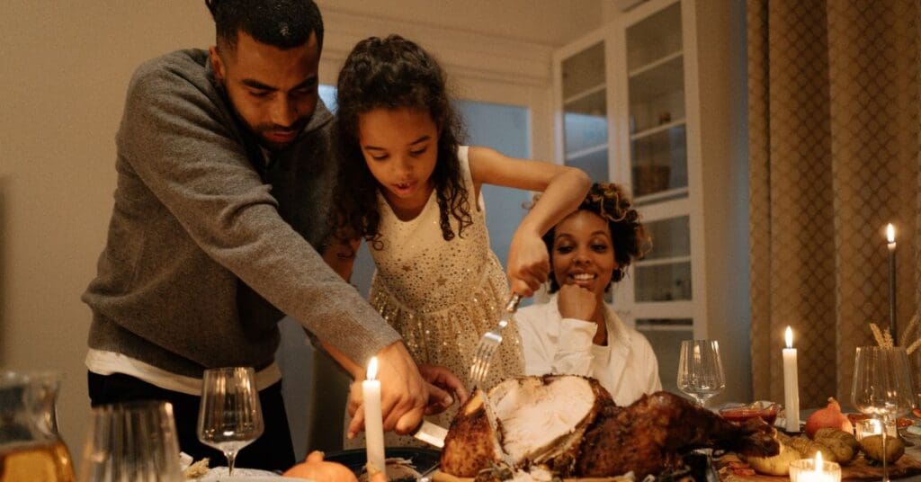 A young girl is helping her father carve a turkey at the dinner table to celebrate Thanksgiving in Canada.