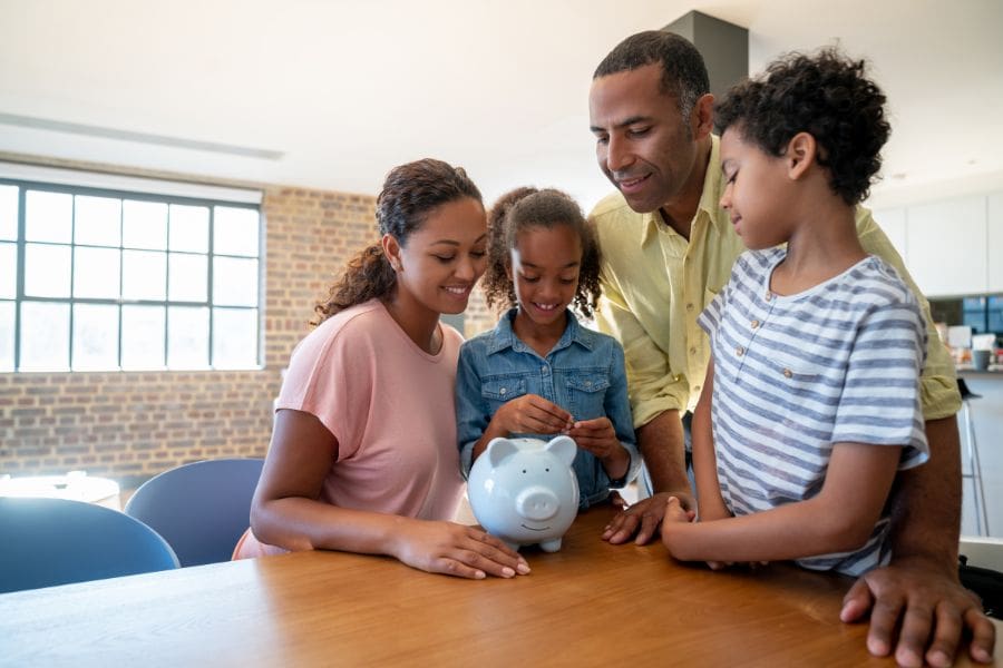 Young children are inserting money into a piggy bank as their parents watch
