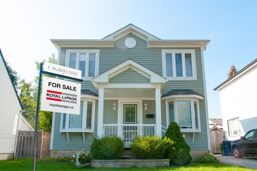 A single-family home in Canada with a “For Sale” sign on the front lawn, representing the Canadian housing market for newcomers.