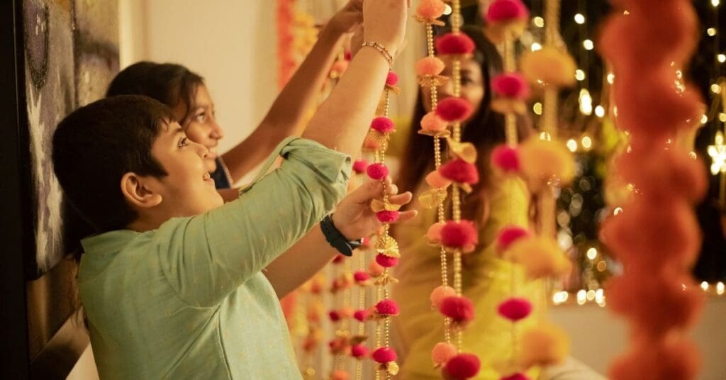 South Asian children hanging colorful marigold garlands and festive decorations inside their home for Diwali.