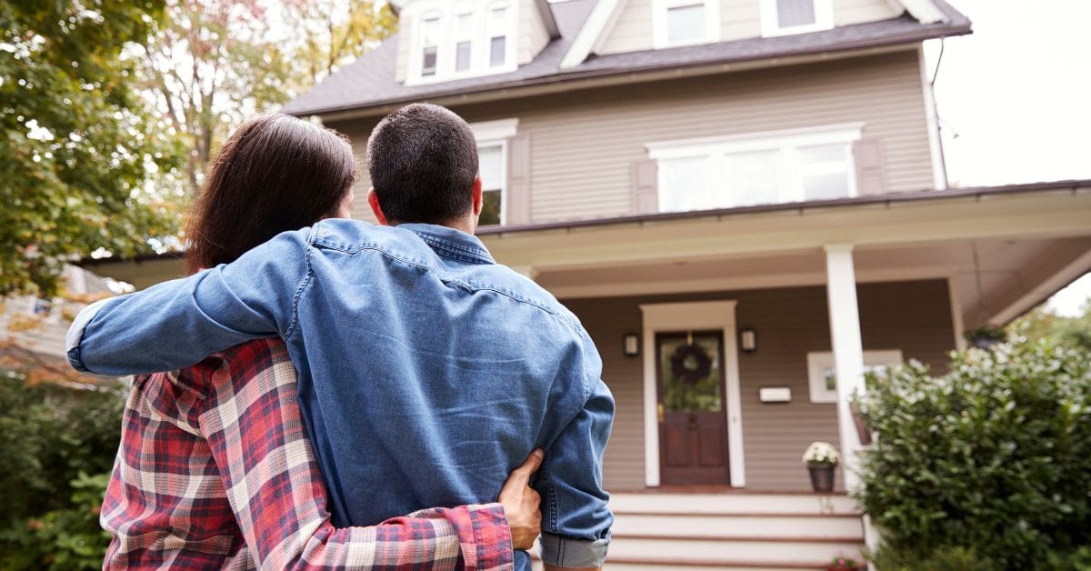 A young couple are looking at the exterior of a home as they decide whether to rent or buy a home in Canada.