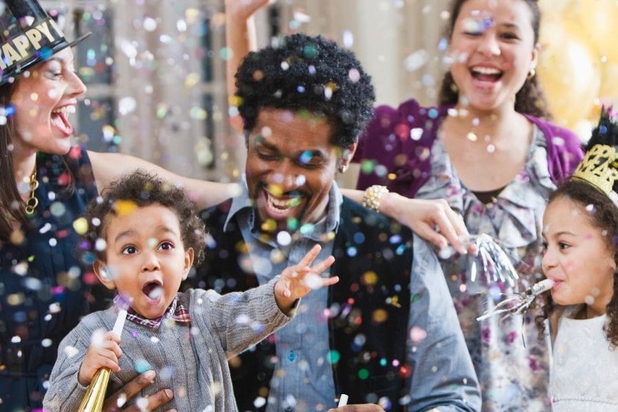 A family with young children celebrating New Year’s Eve at home with party horns and confetti.