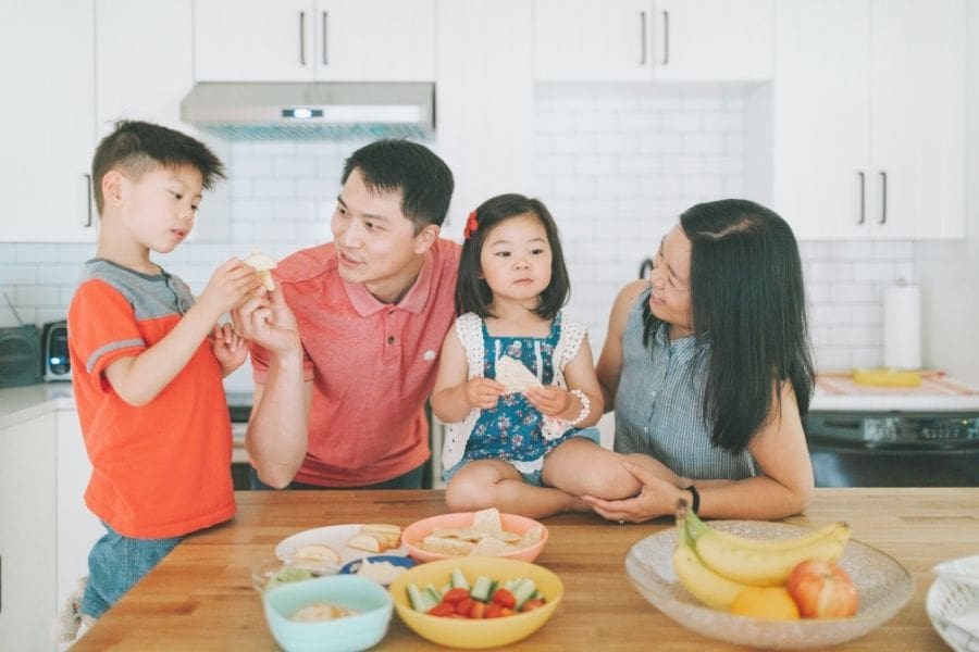 Young family preparing snacks together in the kitchen of a 2-bedroom apartment, showing comfortable shared living space for newcomers.
