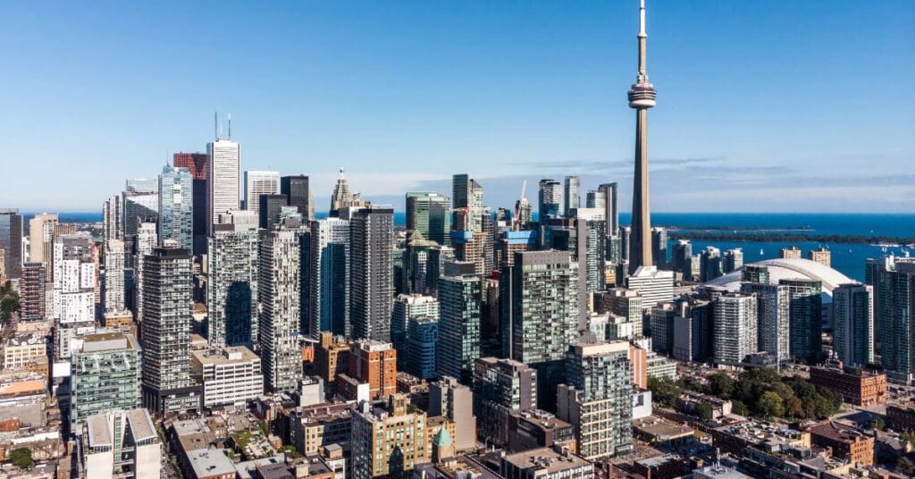 Wide-angle view of the Toronto skyline with the CN Tower and Lake Ontario under a clear blue sky, illustrating the surge in new rental housing supply for 2026.