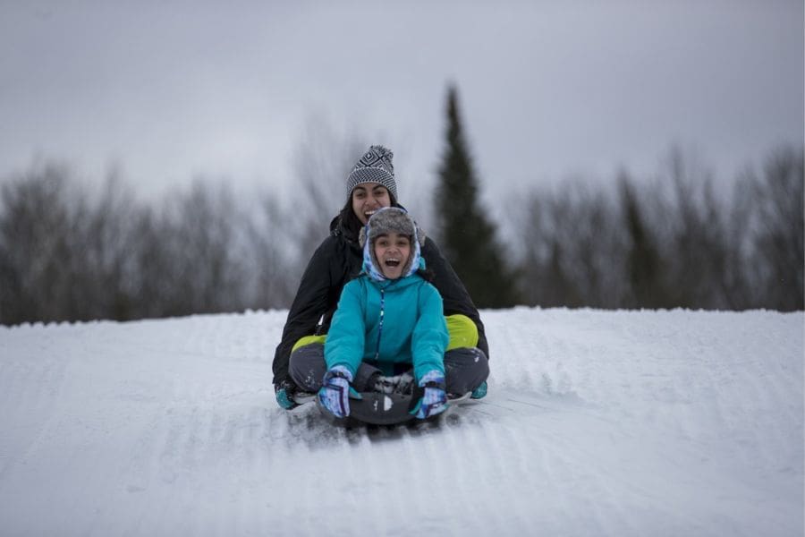 Brother and sister tobogganing down a snowy hill in Canada during March Break.