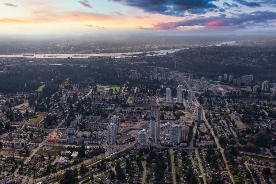 An aerial sunset view of residential neighbourhoods in Burnaby, British Columbia. The SkyTrain transit line leading toward Vancouver is also visible.