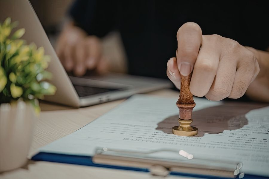 An official is stamping "approval" onto a professional document using a traditional wooden and brass stamp.