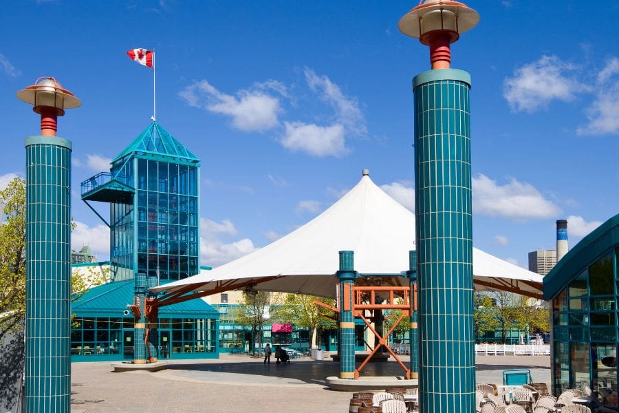 The Forks Market Plaza in Winnipeg features a glass Market Tower, white canopy, and turquoise pillars.