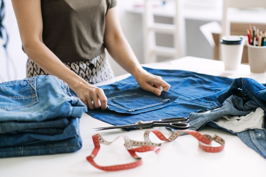 A woman is repairing denim jeans at a repair cafe to resuse and upcycle in the circular economy. 
