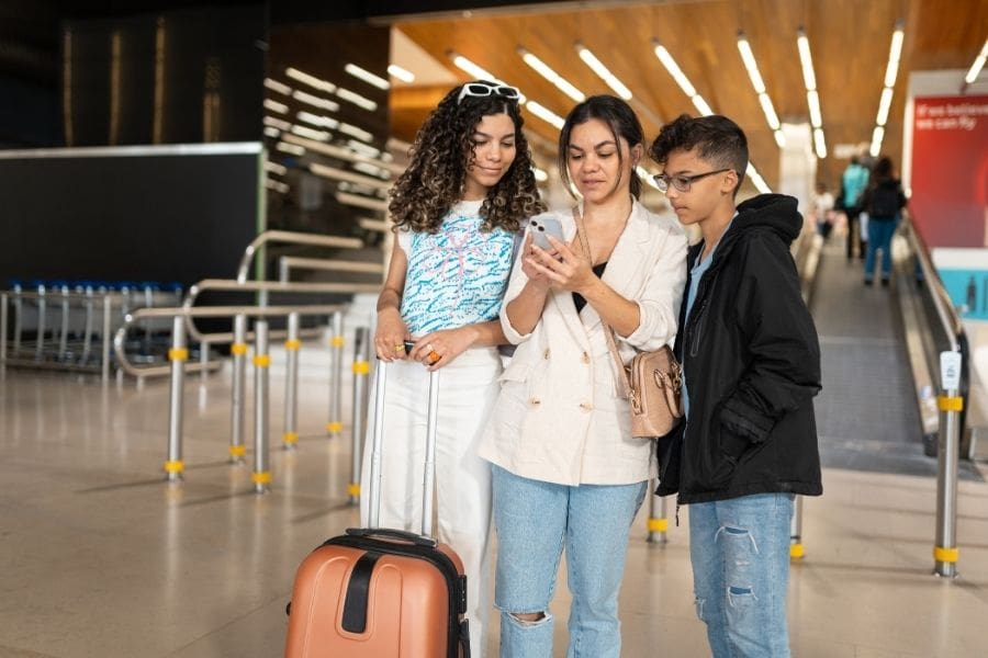 New immigrants checking IRCC application status on mobile phone at the airport with suitcases. 