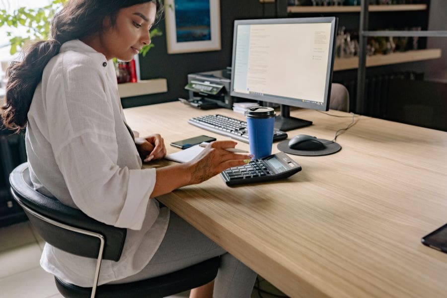 A young woman is using a calculator at a desk to determine the total 2026 Canada PR application fees.
