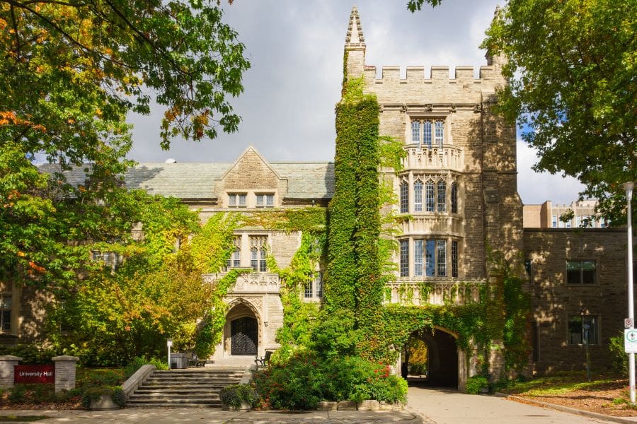 The historic stone facade of University Hall at McMaster University in Hamilton, Ontario, featuring gothic architecture and ivy-covered walls under a bright blue sky.