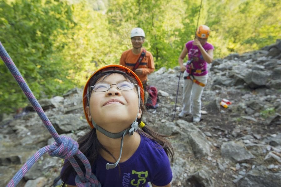 A young girl is looking up while rock climbing on the Niagara Escarpment. Her parents are standing behind her.