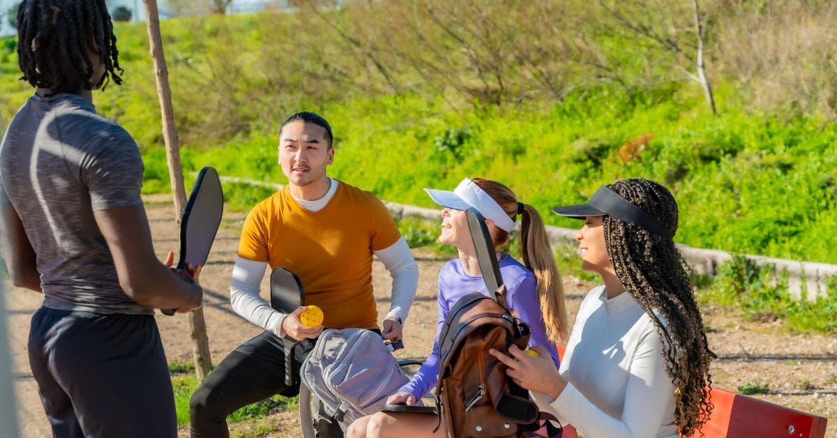 A diverse group of newcomers socializing at a Canadian municipal park after playing pickleball.