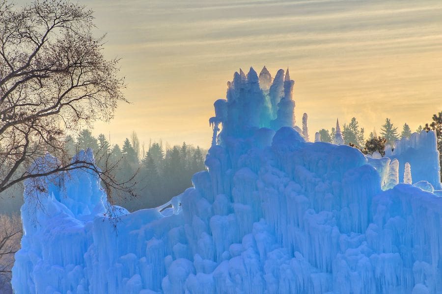 The massive, glowing blue ice castles festival structure at sunset, showing unique winter activities.