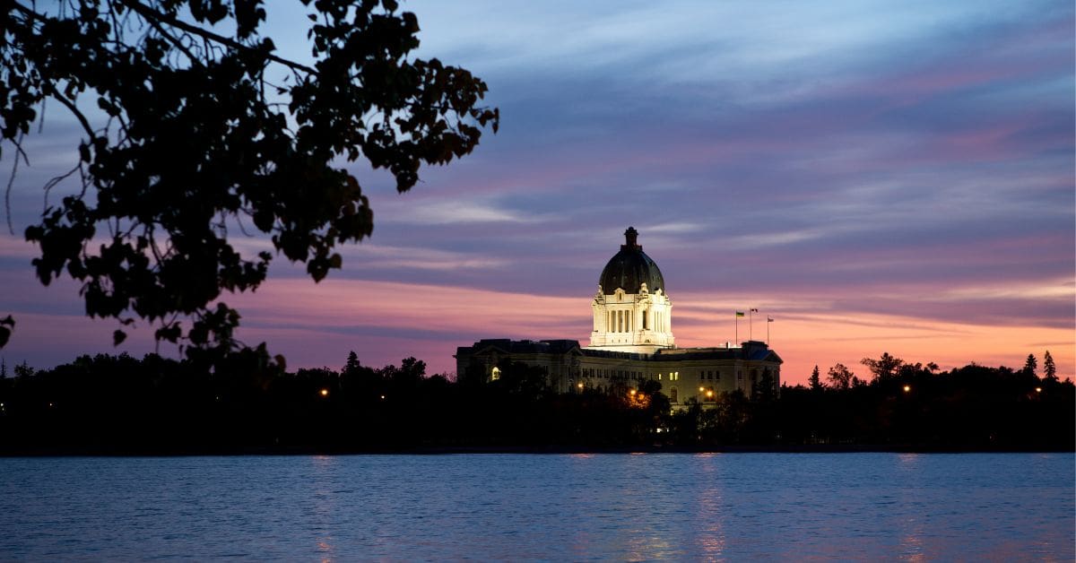 The Saskatchewan Legislative Building illuminated at sunset across Wascana Lake in Regina, Saskatchewan.