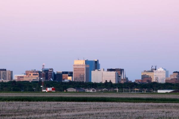The downtown Regina city skyline rising above a vast prairie field at dusk, showing the geography of the area for anyone considering living in Regina.