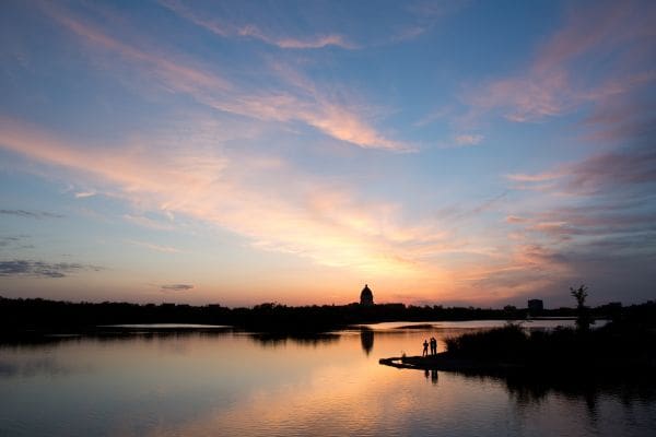 A massive prairie sunset over Wascana Lake with people relaxing by the water, capturing the peaceful lifestyle of living in Regina.