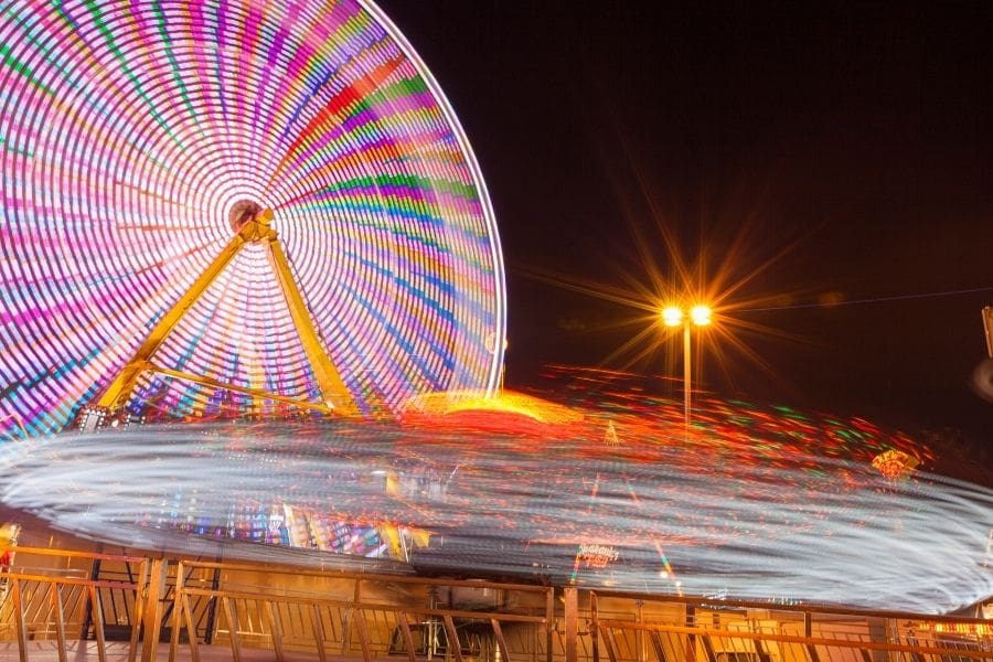 A colourful spinning Ferris wheel and illuminated carnival rides motion blurred at night during a Canadian summer fair.