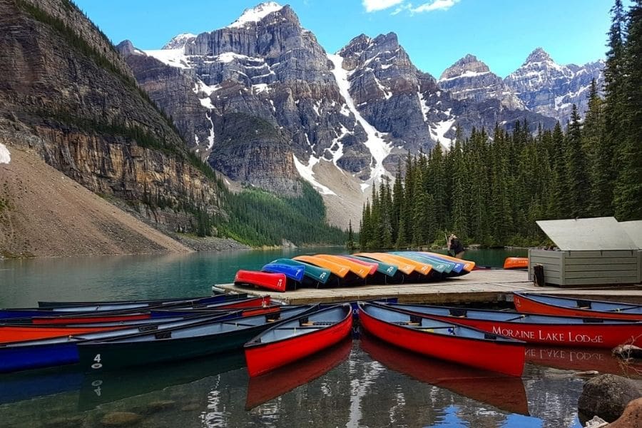 Brightly colored canoes docked on turquoise water at Moraine Lake in Banff, an iconic Parks Canada destination perfect for affordable travel.