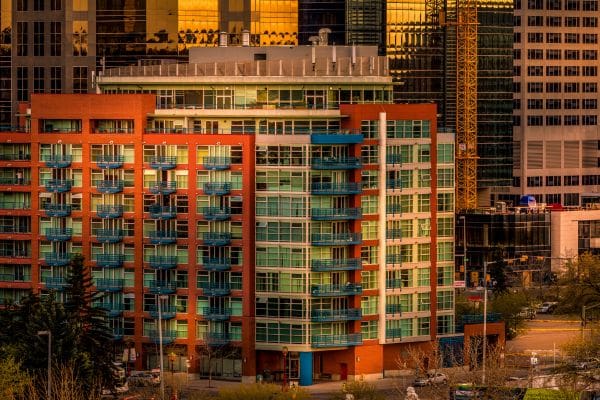 A close-up view of a high-rise residential apartment and condo building in downtown Calgary featuring orange-red brick walls and teal-blue balconies. An ideal snapshot of the housing options available when living in Calgary.