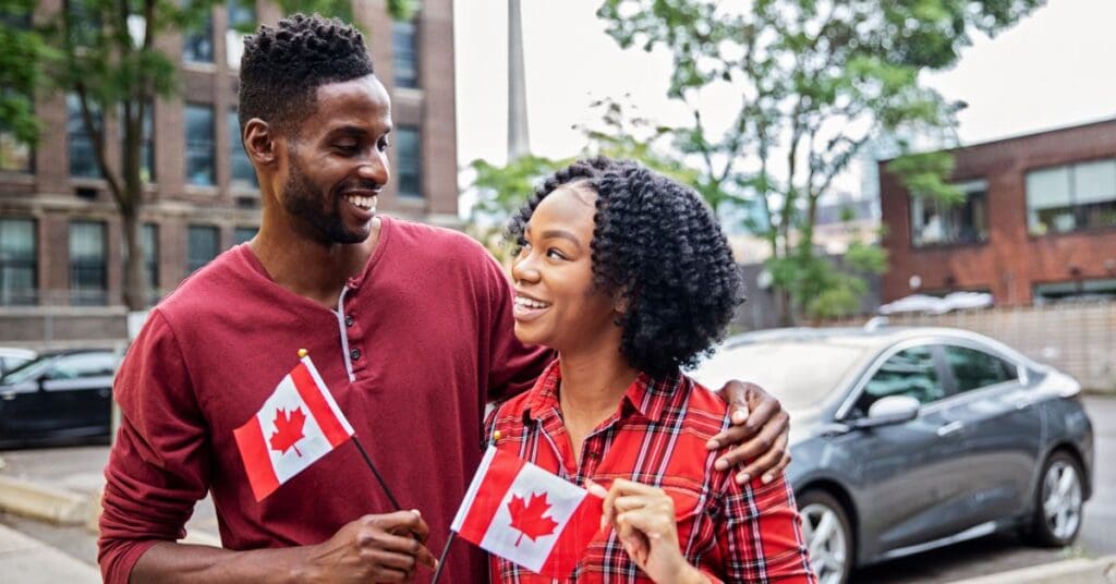 A happy newcomer couple holding Canadian flags in one of the best cities in Canada for immigrants.