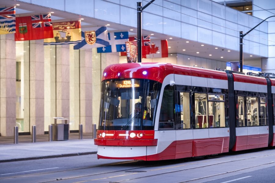 A modern red and white streetcar is passing through the heart of Toronto's financial district. Provincial flags are flying from the Bank of Montreal building. 