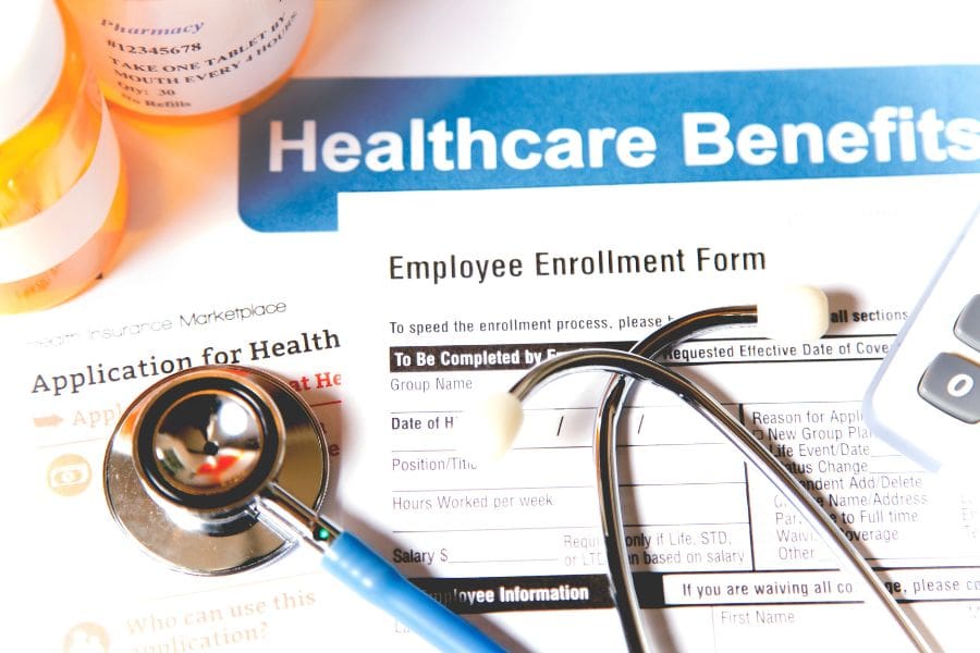 An employee enrollment form for healthcare benefits laid out on a table with a stethoscope, calculator, and prescription pill bottles.