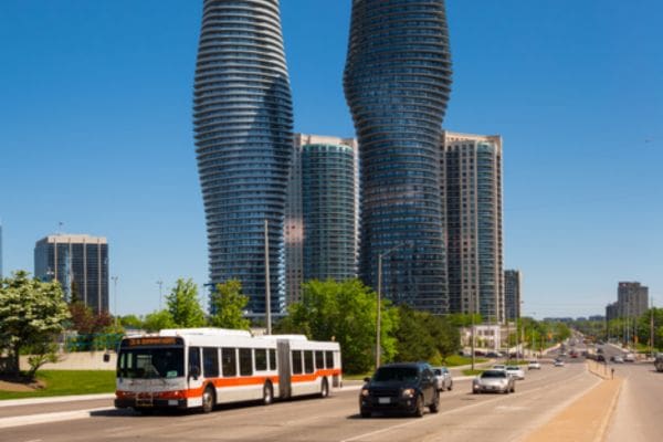 An orange and white MiWay public transit bus driving on Burnhamthorpe Road in downtown Mississauga. The iconic twisting Absolute World towers are in the background.