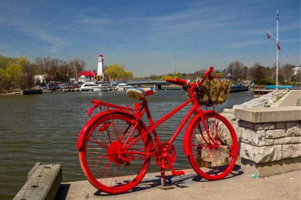 A bright red bicycle is stands upright on the stone walkway at Port Credit marina with the historic lighthouse in the background.