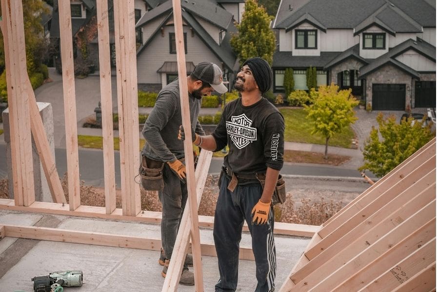 Two immigrant construction workers are smiling while framing a residential home on a building site in Metro Vancouver, British Columbia.